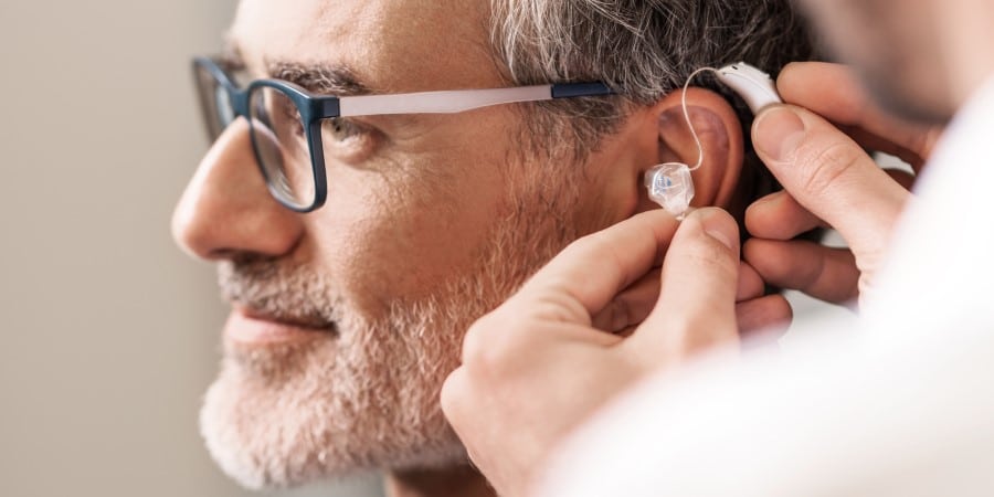 Mann bekommt ein Hinter-dem-Ohr-Hörgerät in das linke Ohr gesetzt.